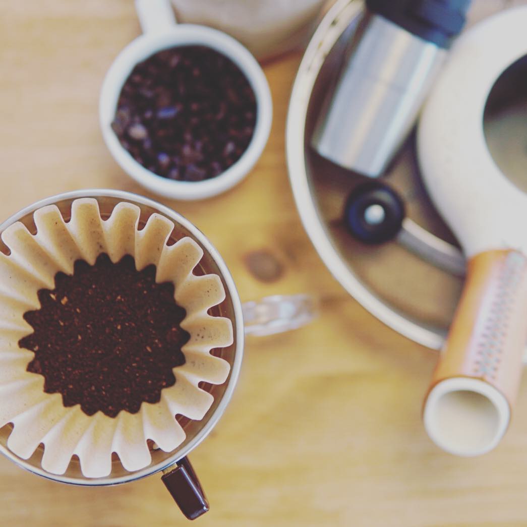 Coffee grounds in a dripper beside Zenroast and a hand grinder